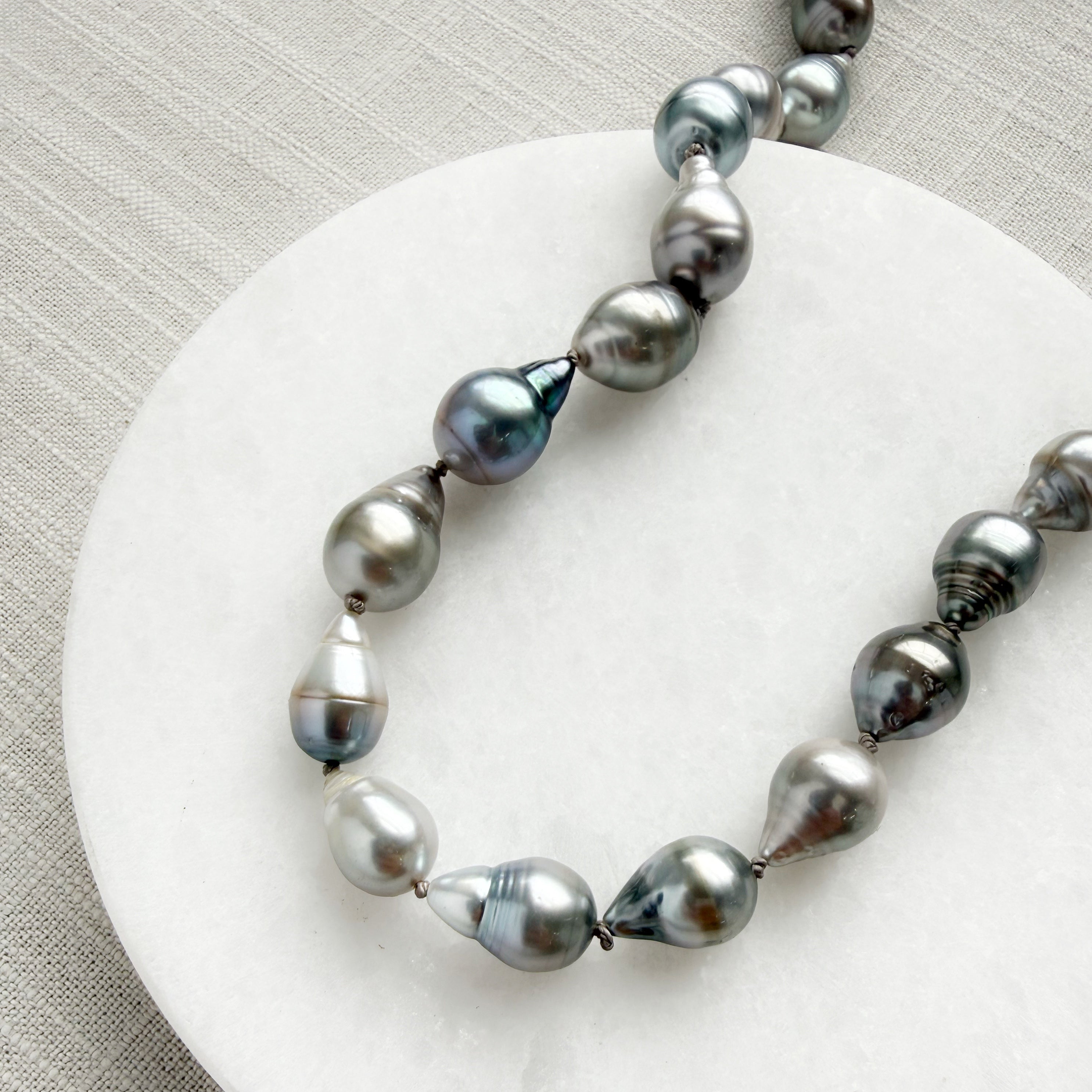 Tahitian pearl necklace on a marble coaster with a textured beige background