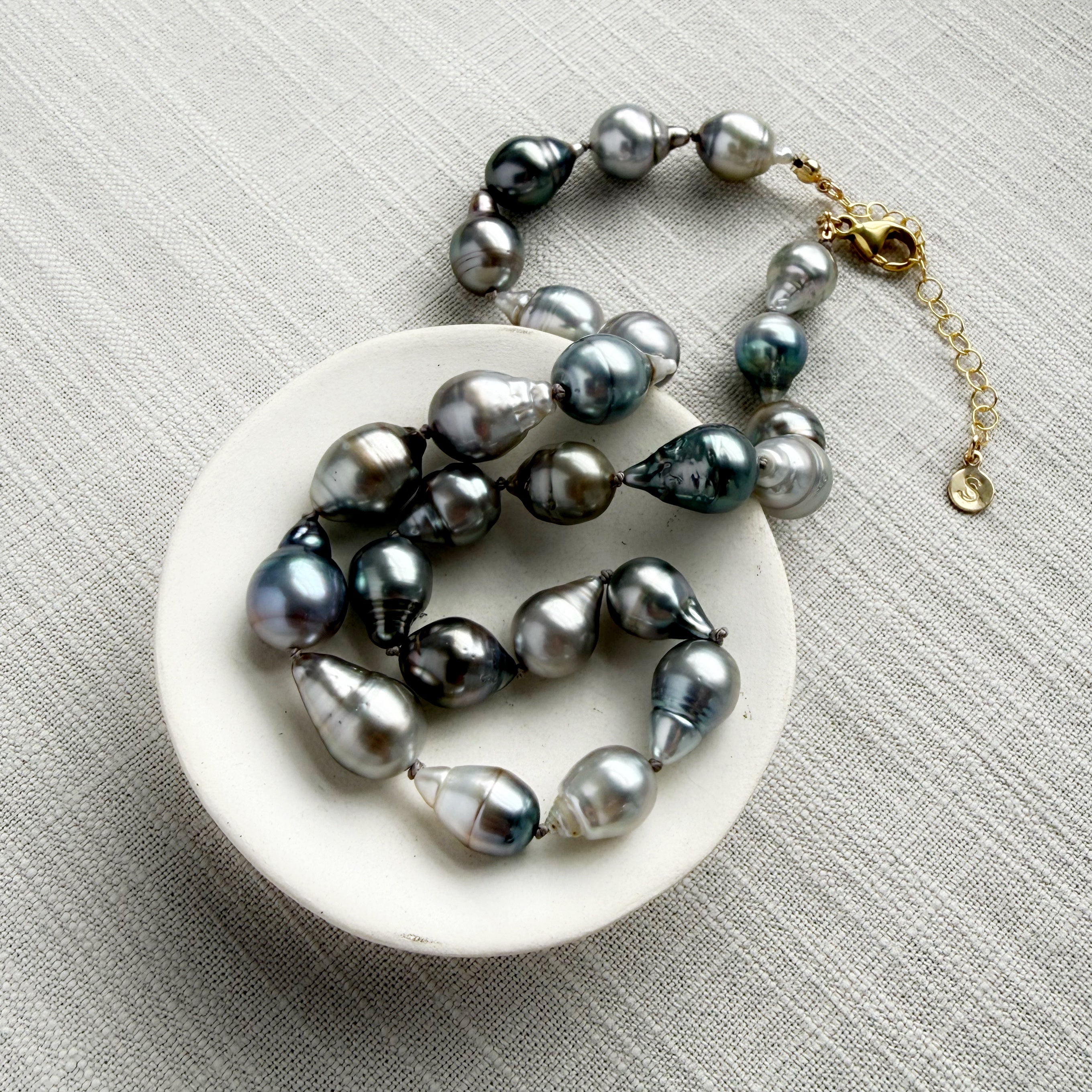 Tahitian pearl necklace on a white dish with a gold clasp on a gray textured background