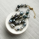 Tahitian pearl necklace on a white dish with a gold clasp on a gray textured background