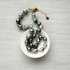 Tahitian pearl necklace on a white dish with a gold clasp on a gray textured background