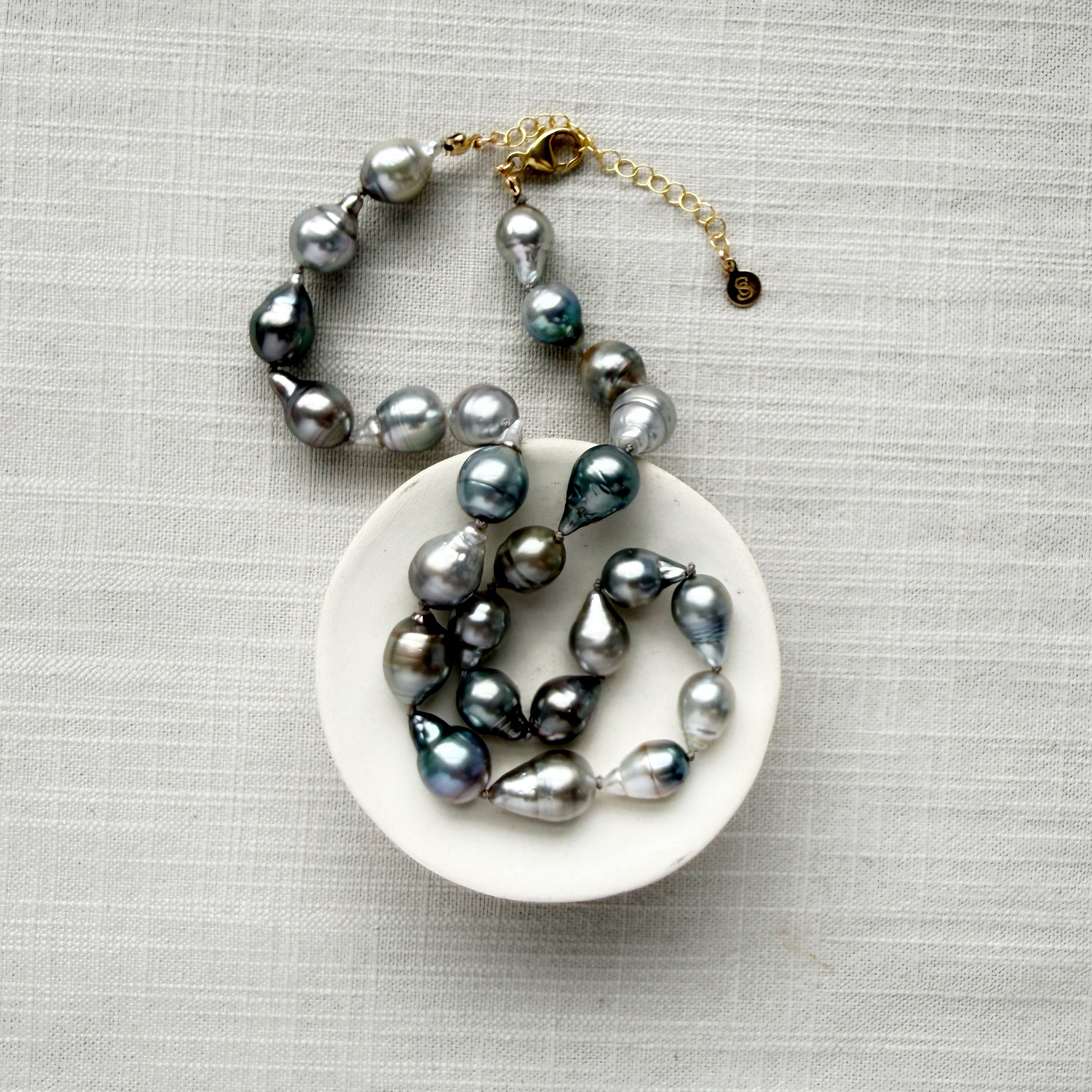 Tahitian pearl necklace on a white dish with a gold clasp on a gray textured background