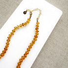 A beaded necklace made of smooth Imperial Topaz with a gold clasp, draped over a small white dish on a textured beige surface.