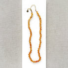 A beaded necklace made of smooth Imperial Topaz with a gold clasp, draped over a small white dish on a textured beige surface.