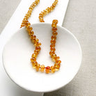 A beaded necklace made of smooth Imperial Topaz with a gold clasp, draped over a small white dish on a textured beige surface.