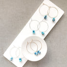 Three pairs of hoop earrings with small Golden Hills Turquoise beads, displayed on a white jewelry stand against a textured gray background.
