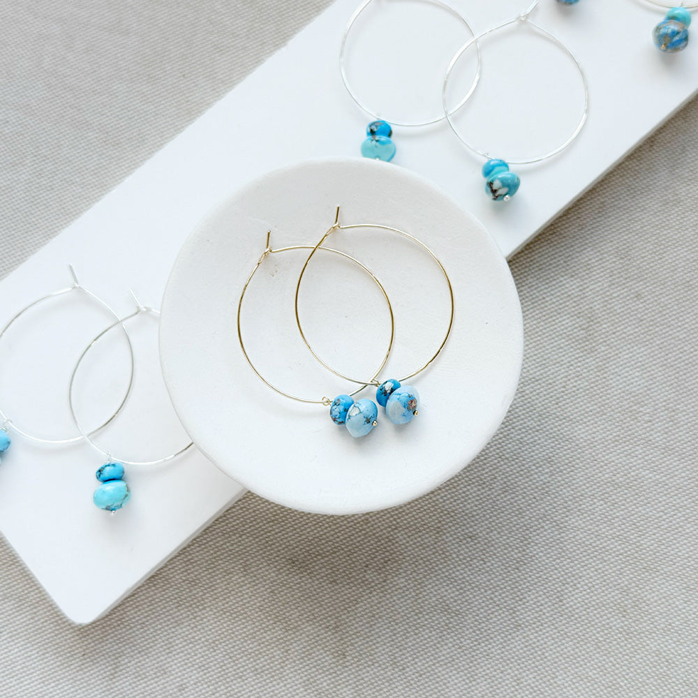 Pairs of hoop earrings with small Golden Hills Turquoise beads, displayed on a white card against a textured gray background.
