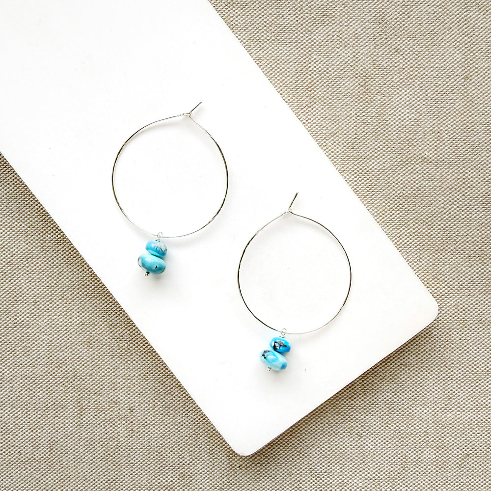 Pair of hoop earrings with small Golden Hills Turquoise beads, displayed on a white card against a textured gray background.