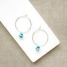 Pair of hoop earrings with small Golden Hills Turquoise beads, displayed on a white card against a textured gray background.