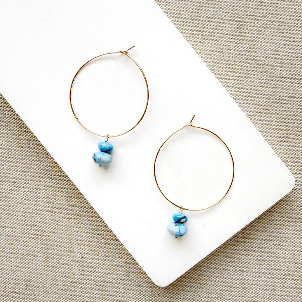 Pair of hoop earrings with small Golden Hills Turquoise beads, displayed on a white card against a textured gray background.