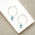 Pair of hoop earrings with small Golden Hills Turquoise beads, displayed on a white card against a textured gray background.