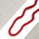 A coral knotted necklace in a rich red color with a gold clasp, displayed on a white ceramic dish over a light gray textured fabric background.