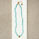 Turquoise beaded necklace with gold accents on a beige background
