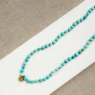 Turquoise beaded necklace with gold accent on a white and beige surface