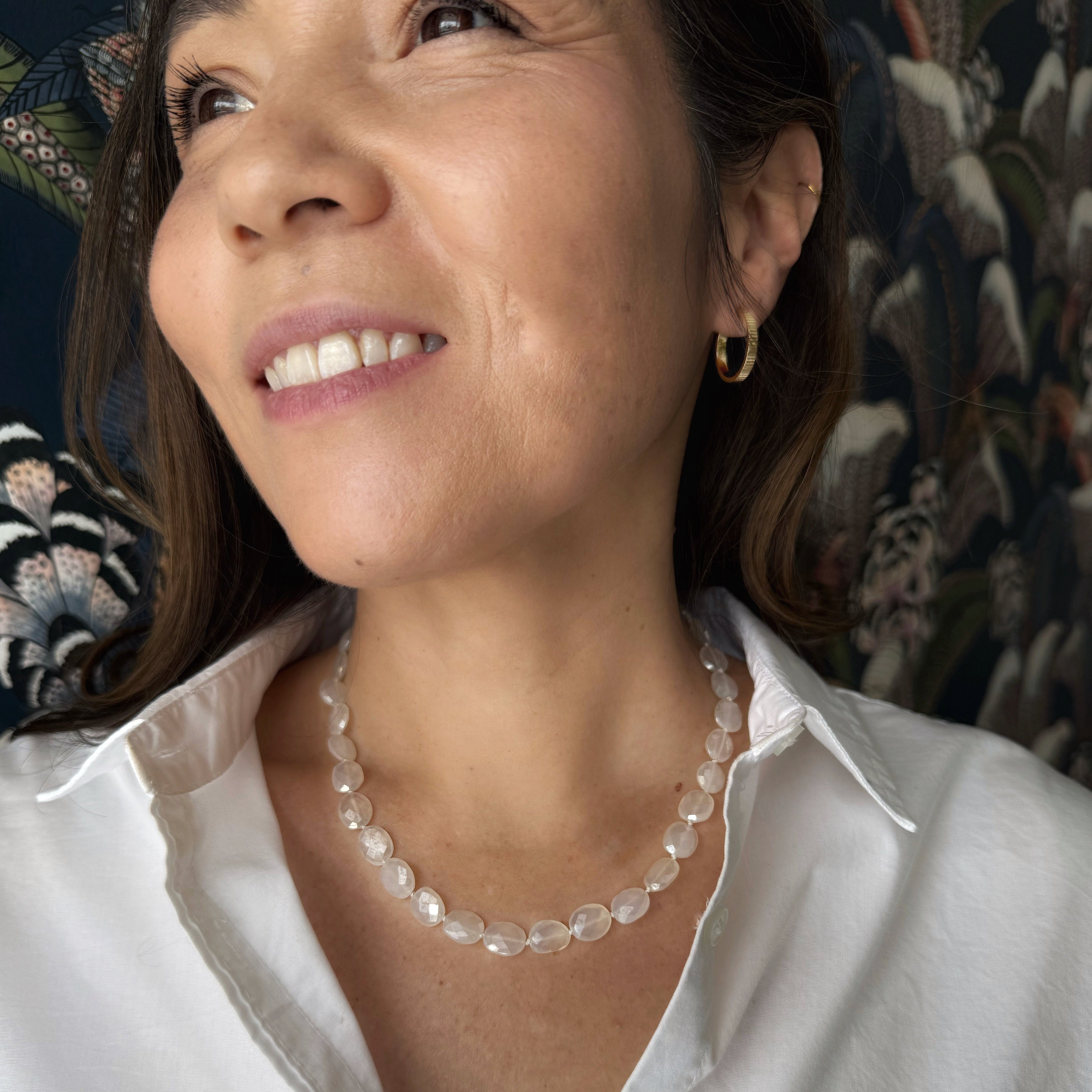 Woman wearing a white shirt and white chalcedony necklace with a floral background