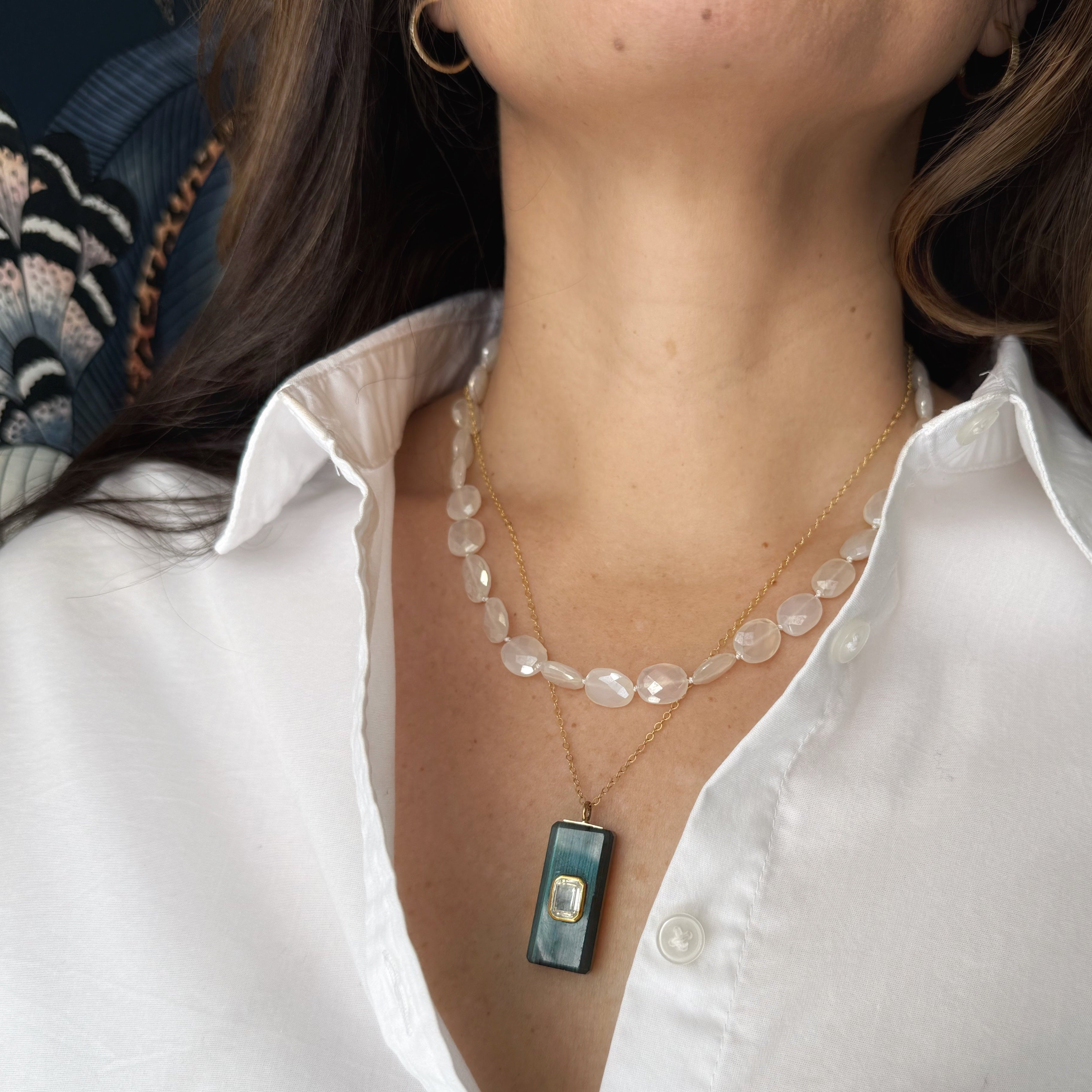 Person wearing a white shirt with a white chalcedony necklace and a rectangular pendant.