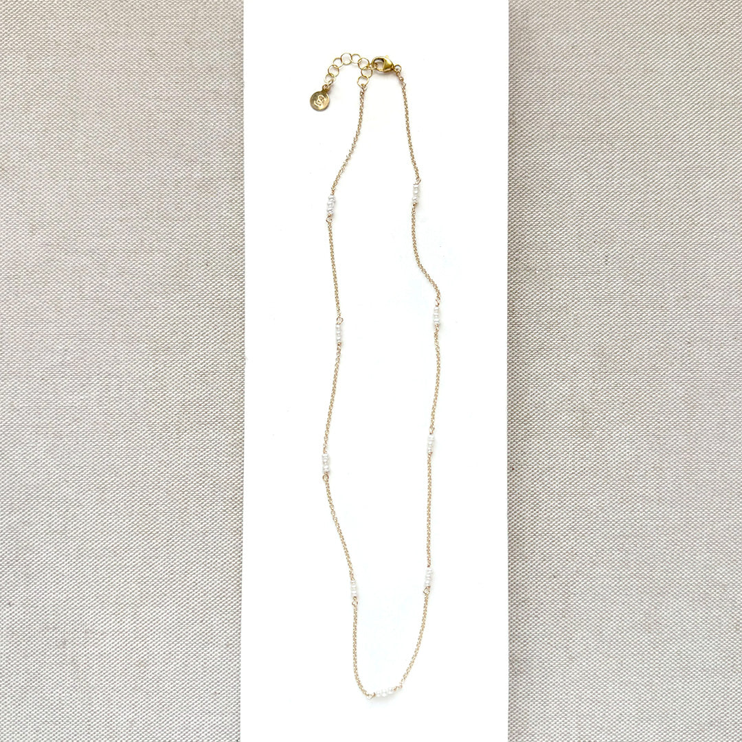 Delicate gold necklace with small white pearls on a light gray fabric background