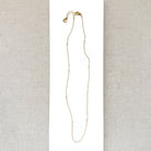Delicate gold necklace with small white pearls on a light gray fabric background