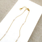 Clasp detail of gold necklace with small pearls on a textured surface