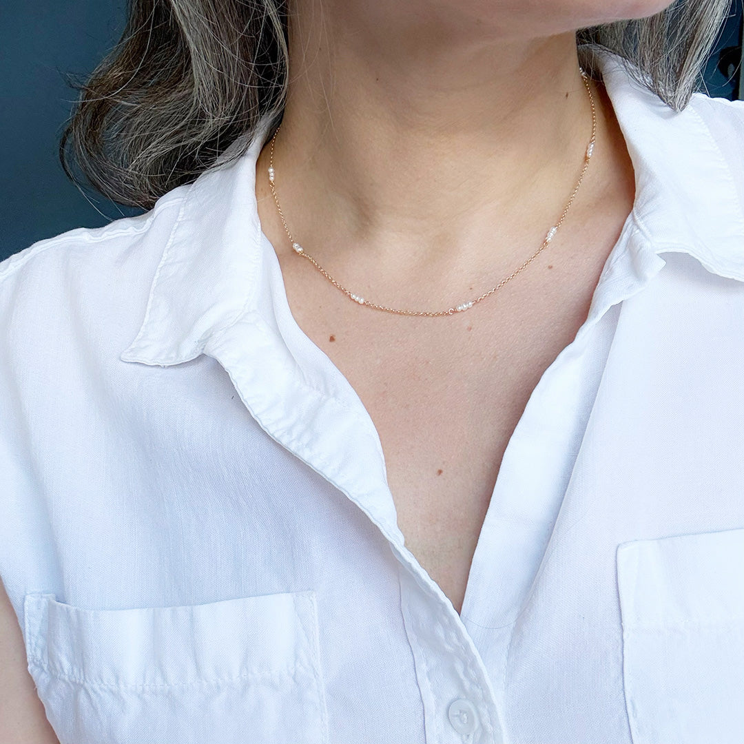 Person wearing a delicate gold and pearl necklace with a white shirt against a blue background