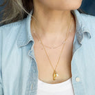 Person wearing a gold and pearl necklace layered with a pendant and pearl, layered with other necklaces, against a denim jacket.