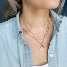 Person wearing multiple gold necklaces with a denim shirt