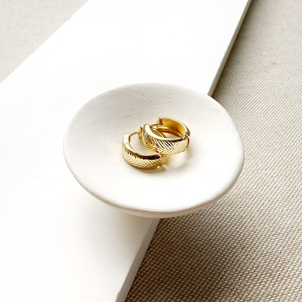 Textured solid gold hoops in a white dish