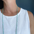 Woman wearing white tank and a long knotted turquoise necklace on a navy background