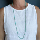 Woman wearing white tank and a long knotted turquoise necklace on a navy background