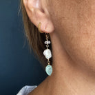 Close-up of an ear wearing a set of earrings with green gemstones against a dark background.