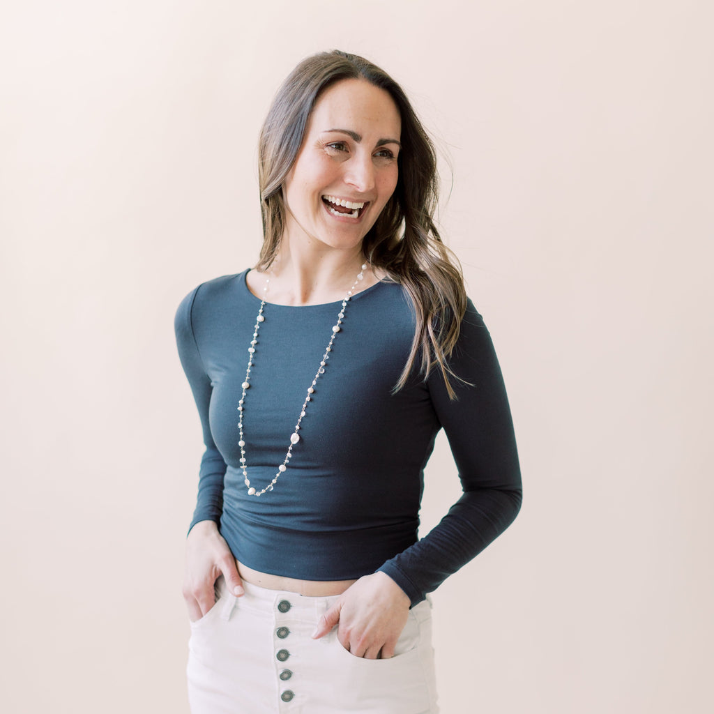 Woman with long dark hair wearing black shirt and white pants with gold, pearl and gemstone long statement pearl necklace with wire wrapped moonstone, white chalcedony, white topaz, and freshwater pearls and gold ball stud earrings. Poppy Linen necklace by Sarah Cornwell Jewelry