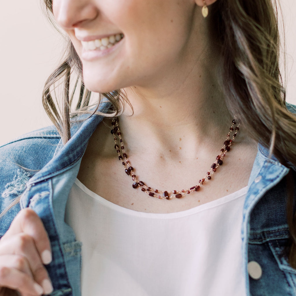 Woman's neckline with doubled gold and garnet long statement gemstone necklace with wire wrapped garnet gemstones and tiny gold textured disc earrings. Poppy Garnet Necklace by Sarah Cornwell Jewelry