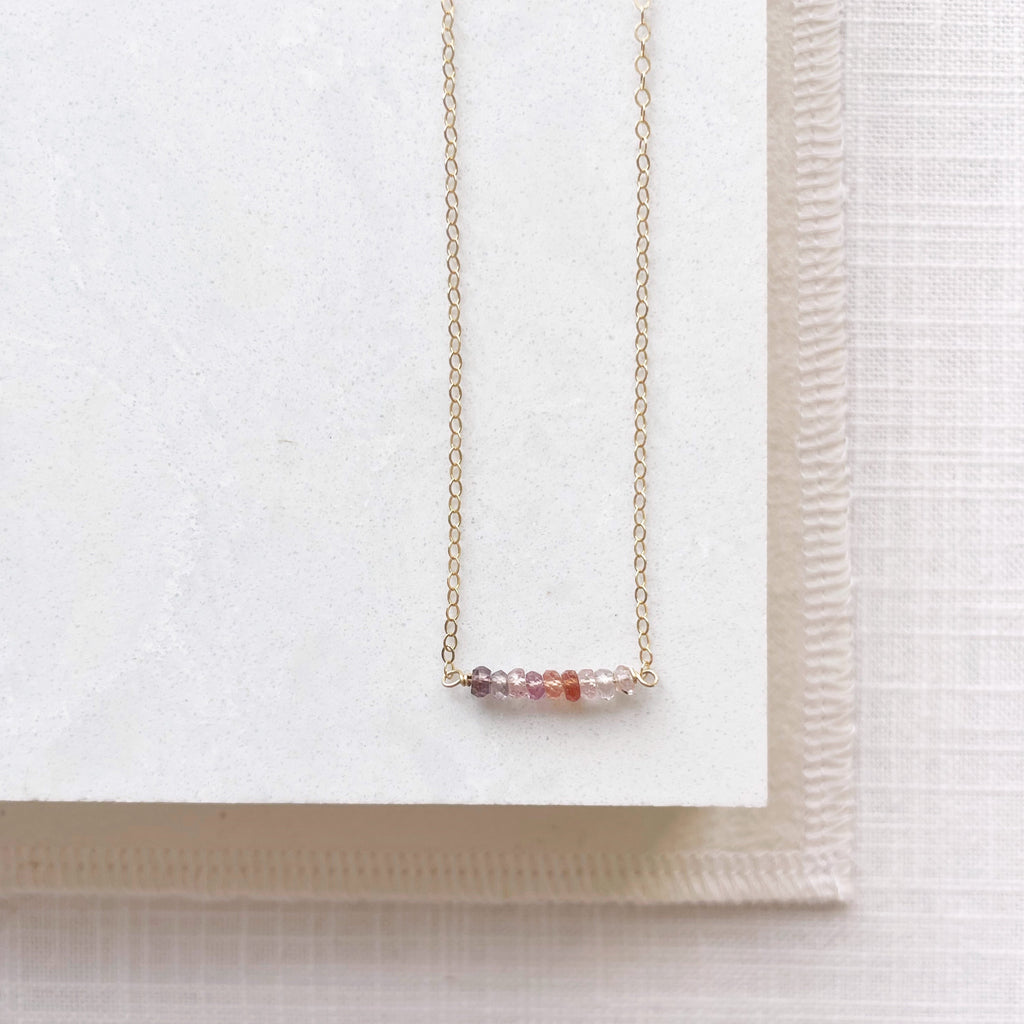 Dainty gold 16 inch gemstone necklace with sapphires in warm shades on a straight bar. Andra necklace by Sarah Cornwell Jewelry