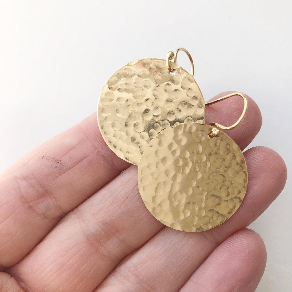 Gold Buffay Earrings by Sarah Cornwell Jewelry. Hand holding lightweight, shimmery, textured 1 inch gold disc earrings on a white background.