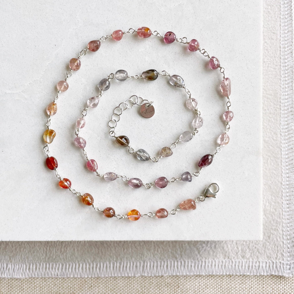 17 inch silver and gemstone necklace laid out in a spiral with a full strand of wire wrapped gradient colored red, purple and pink spinel gemstones. Cain Necklace by Sarah Cornwell Jewelry