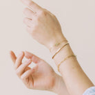 Close up of woman's wrists wearing gold textured bangle bracelet, gold textured disc bracelet and gold chunky link chain bracelet. Caroline Bangle by Sarah Cornwell Jewelry