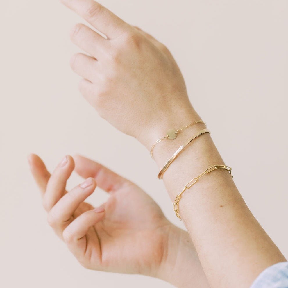 Close up of woman's wrists wearing gold textured bangle bracelet, gold textured disc bracelet and gold chunky link chain bracelet. Caroline Bangle by Sarah Cornwell Jewelry