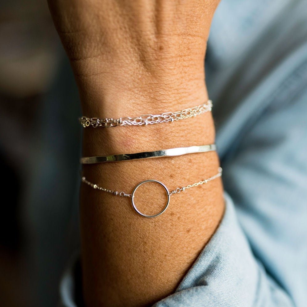 Close up of woman's wrist wearing silver textured bangle bracelet, silver circle bracelet and silver multi chain bracelet. Caroline Bangle by Sarah Cornwell Jewelry