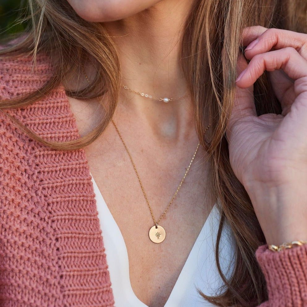 Woman with long hair wearing a pink sweater with a gold dainty pearl layering necklace, gold dandelion disc layering necklace and gold bracelet. Carys Necklace by Sarah Cornwell Jewelry