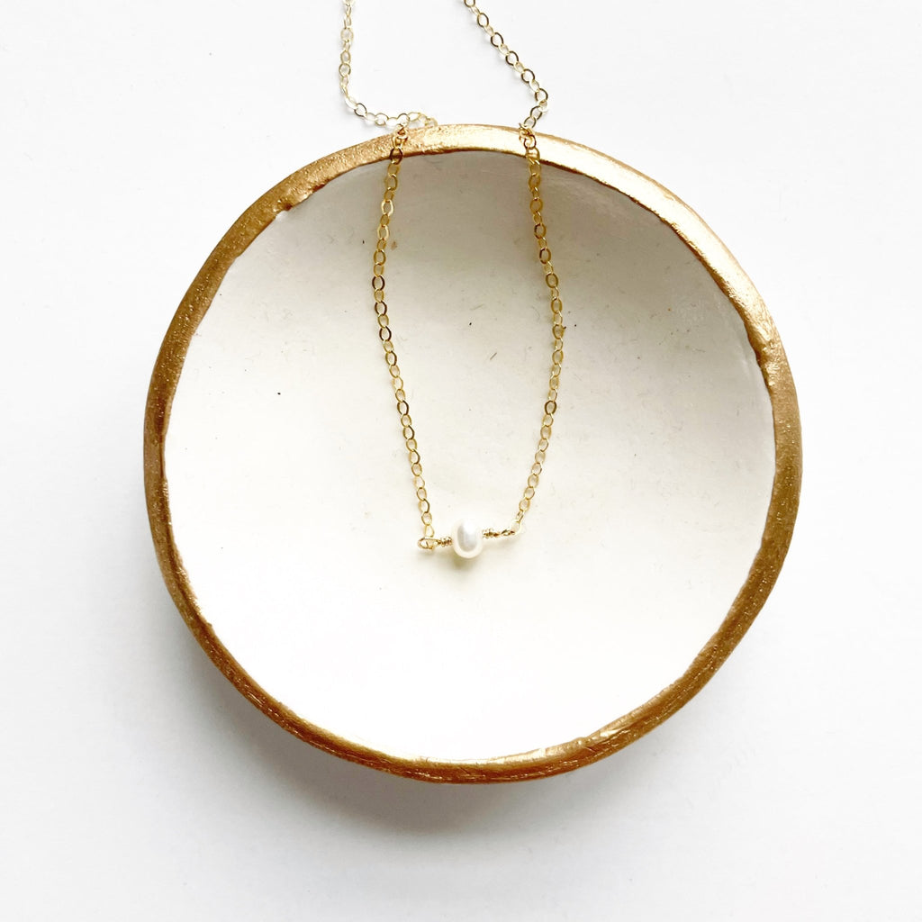 Gold dainty pearl layering necklace in a white and gold dish. Carys Necklace by Sarah Cornwell Jewelry
