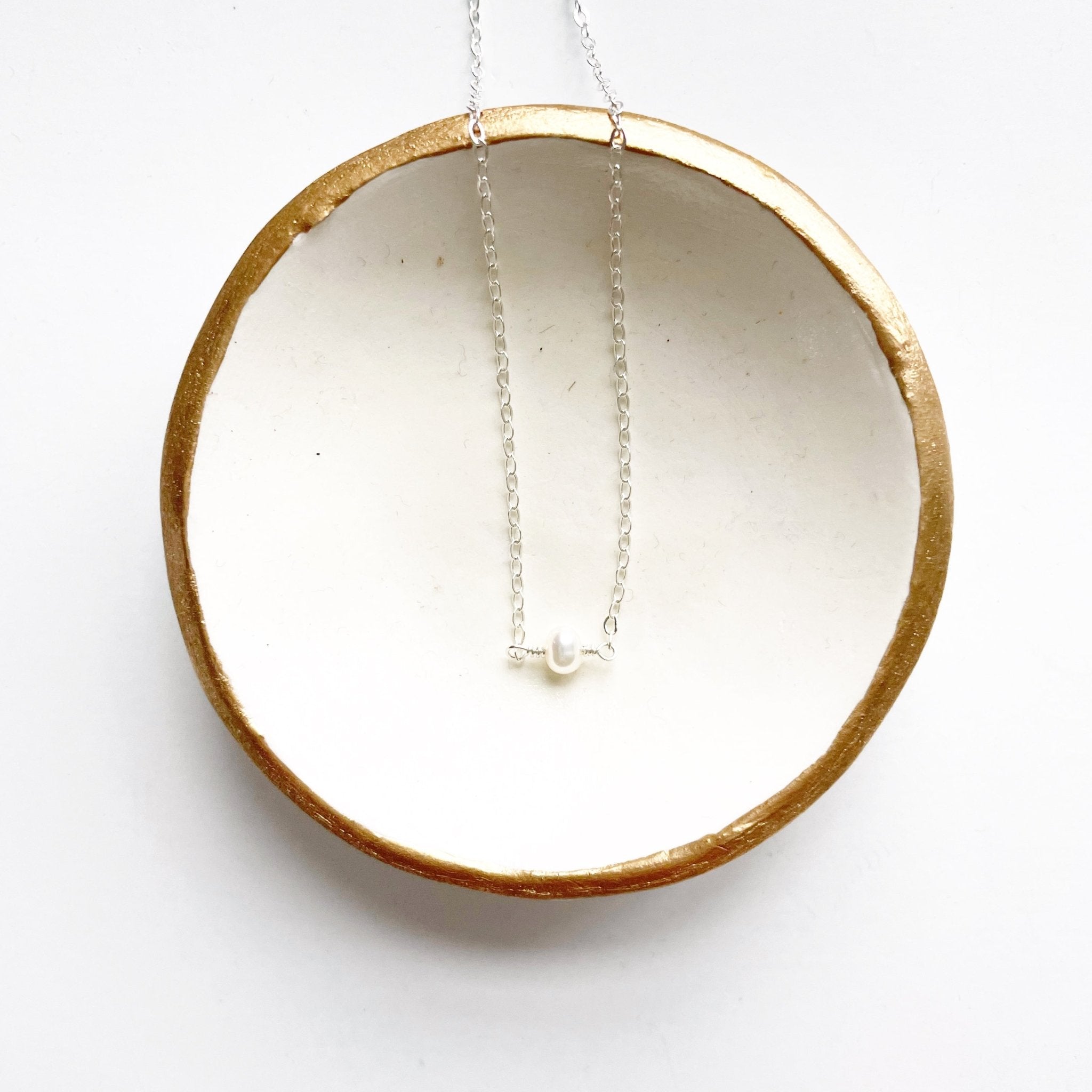 Silver dainty pearl layering necklace in a white and gold dish. Carys Necklace by Sarah Cornwell Jewelry
