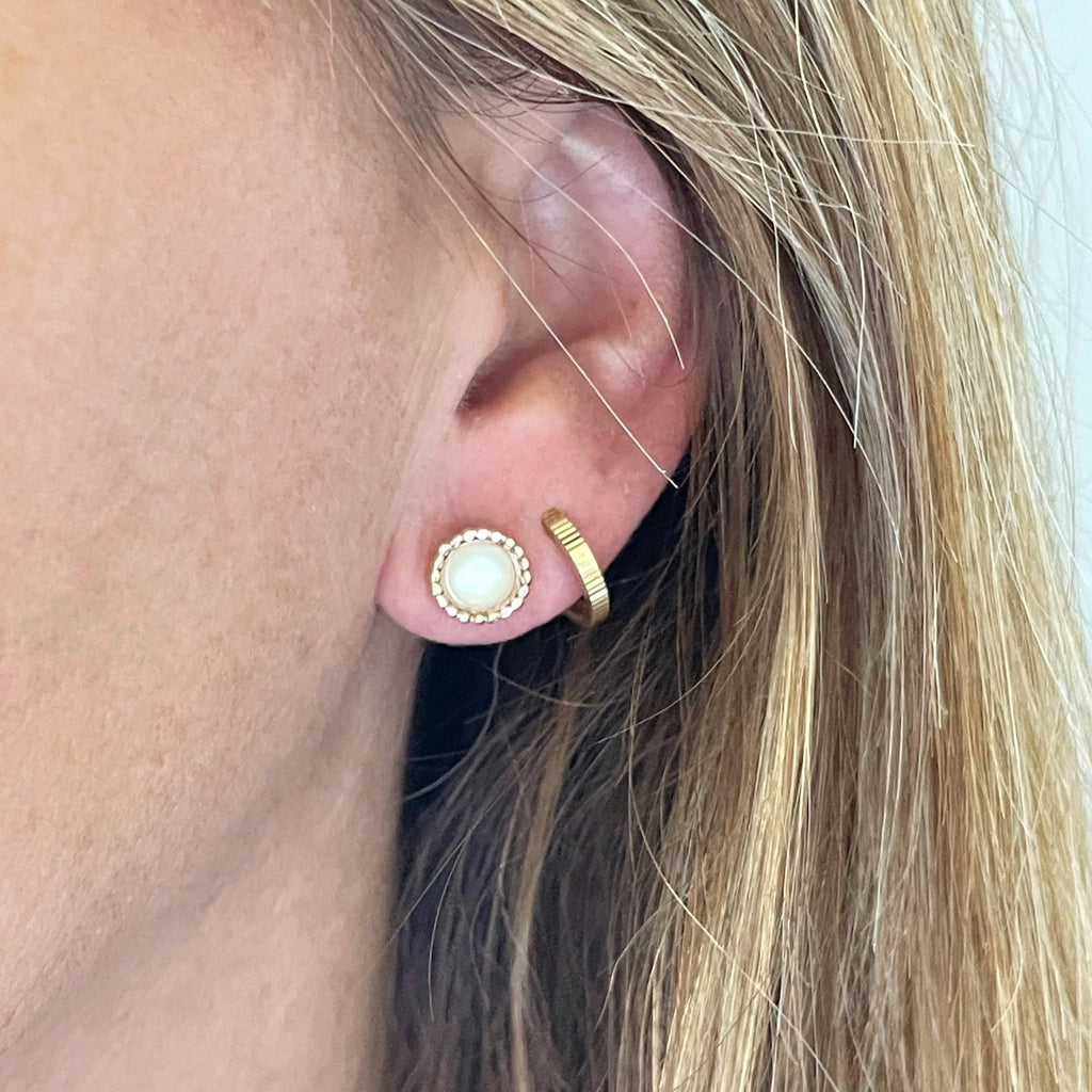 Close up of blonde haired woman wearing 6mm gold and mother of pearl stud earrings with a beaded bezel setting and a gold huggie hoop earring in second piercing.. Chantilly Studs by Sarah Cornwell Jewelry