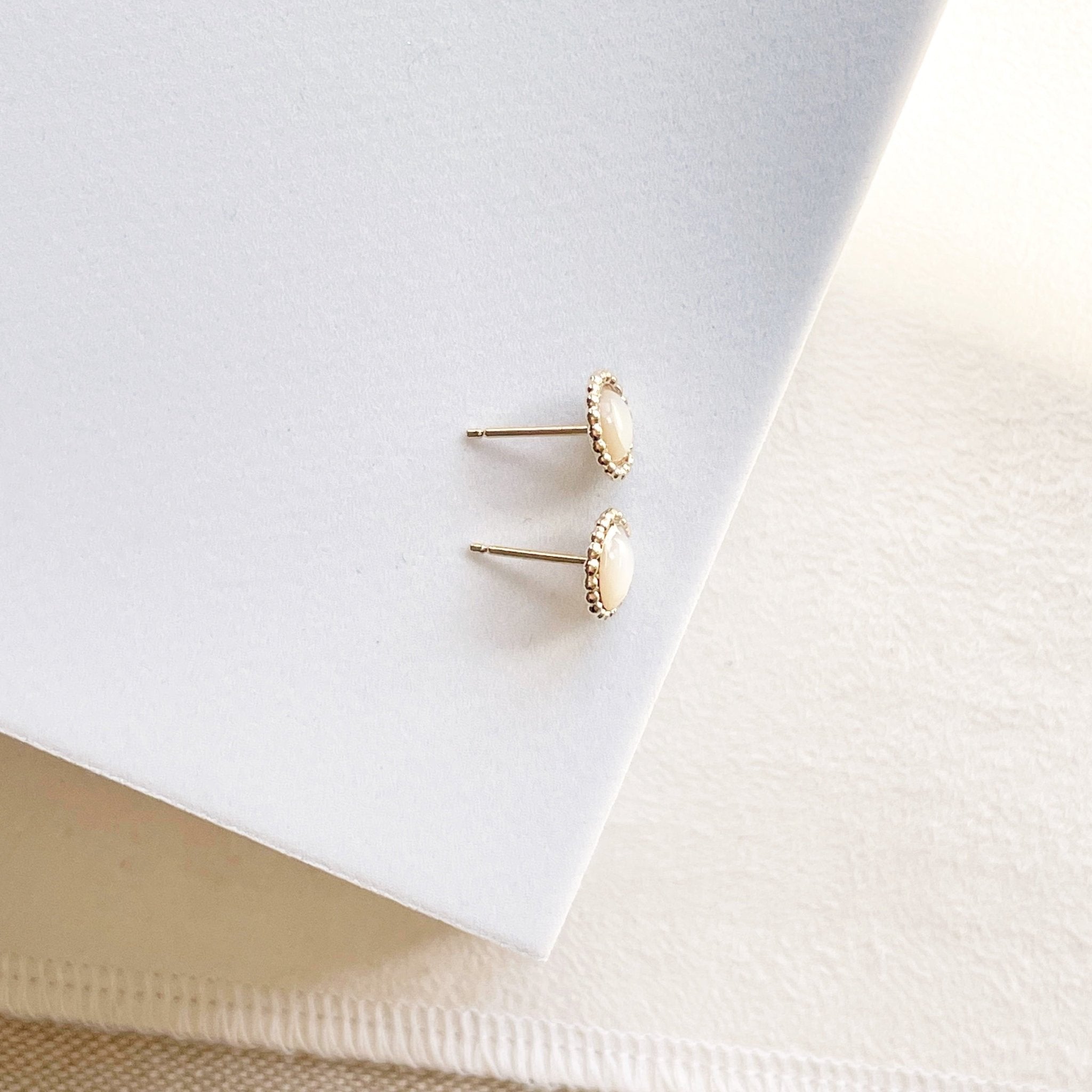 Side view of 6mm gold and mother of pearl stud earrings with a beaded bezel setting. Chantilly Studs by Sarah Cornwell Jewelry