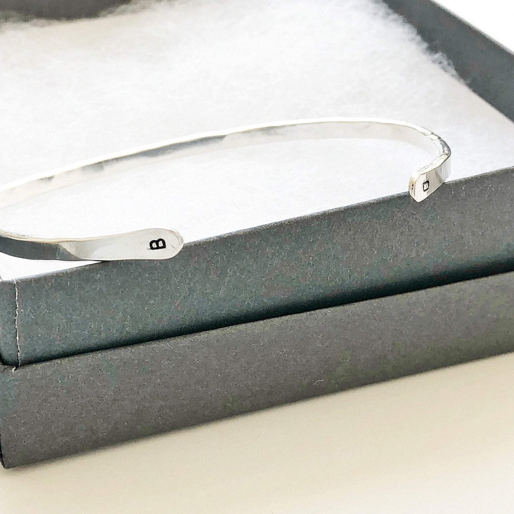 Silver textured bangle bracelet with initials stamped on both ends in a gray gift box. Charlie Bangle by Sarah Cornwell Jewelry
