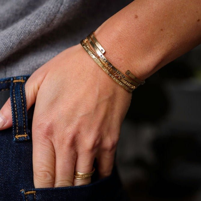 Woman's wrist wearing gray sweater and jeans with 3 gold textured bangle bracelets with initials stamped on both ends. Charlie Bangle by Sarah Cornwell Jewelry