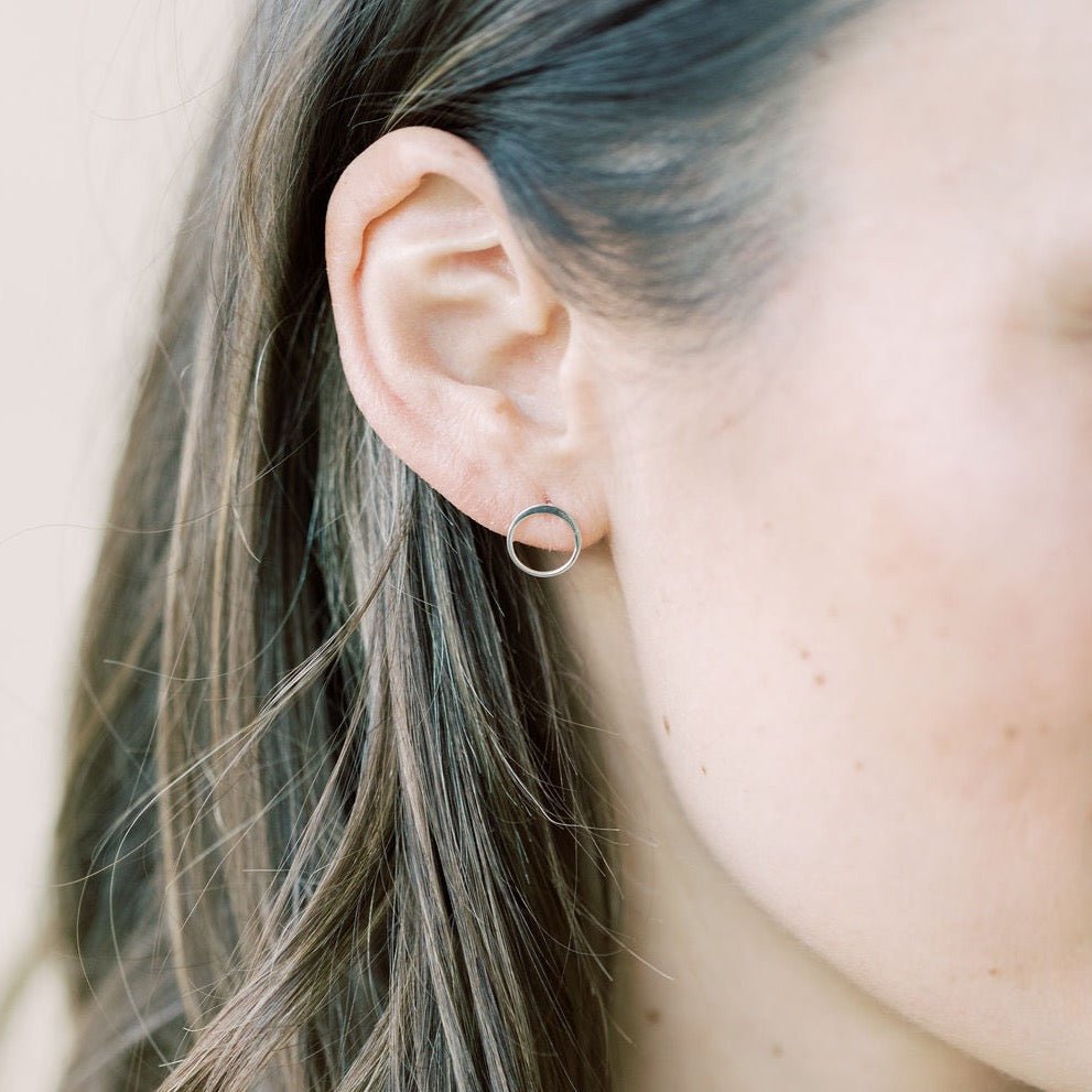 Close up side view of woman with long brown hair wearing silver simple circle stud earrings. Circle Studs by Sarah Cornwell Jewelry