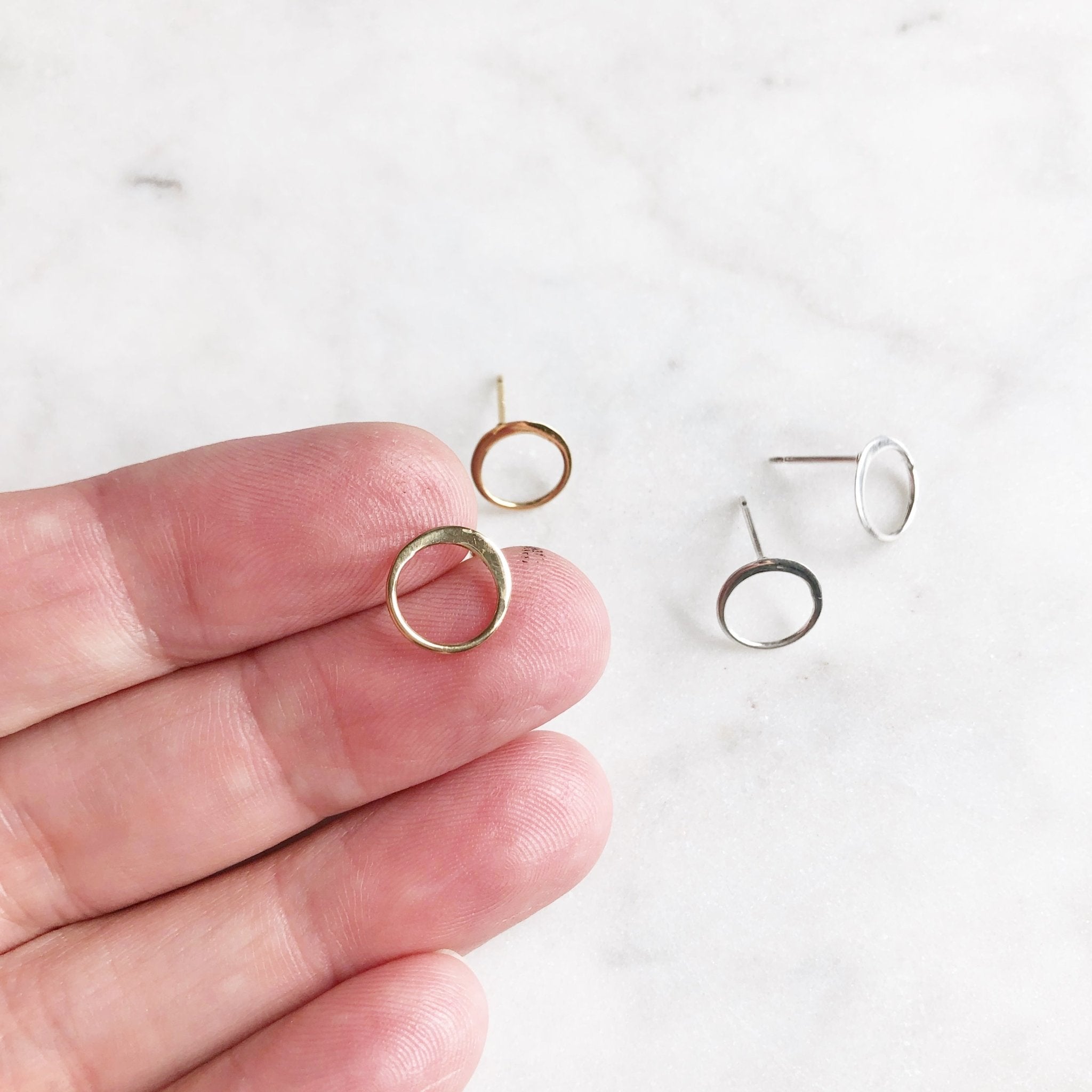 Close up of gold and silver simple circle stud earrings. Hand holding one earring.Circle Studs by Sarah Cornwell Jewelry