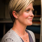 Side view of woman with short blonde hair wearing a gray sweater with gold simple circle stud earrings and layered gemstone necklaces. Circle Studs by Sarah Cornwell Jewelry