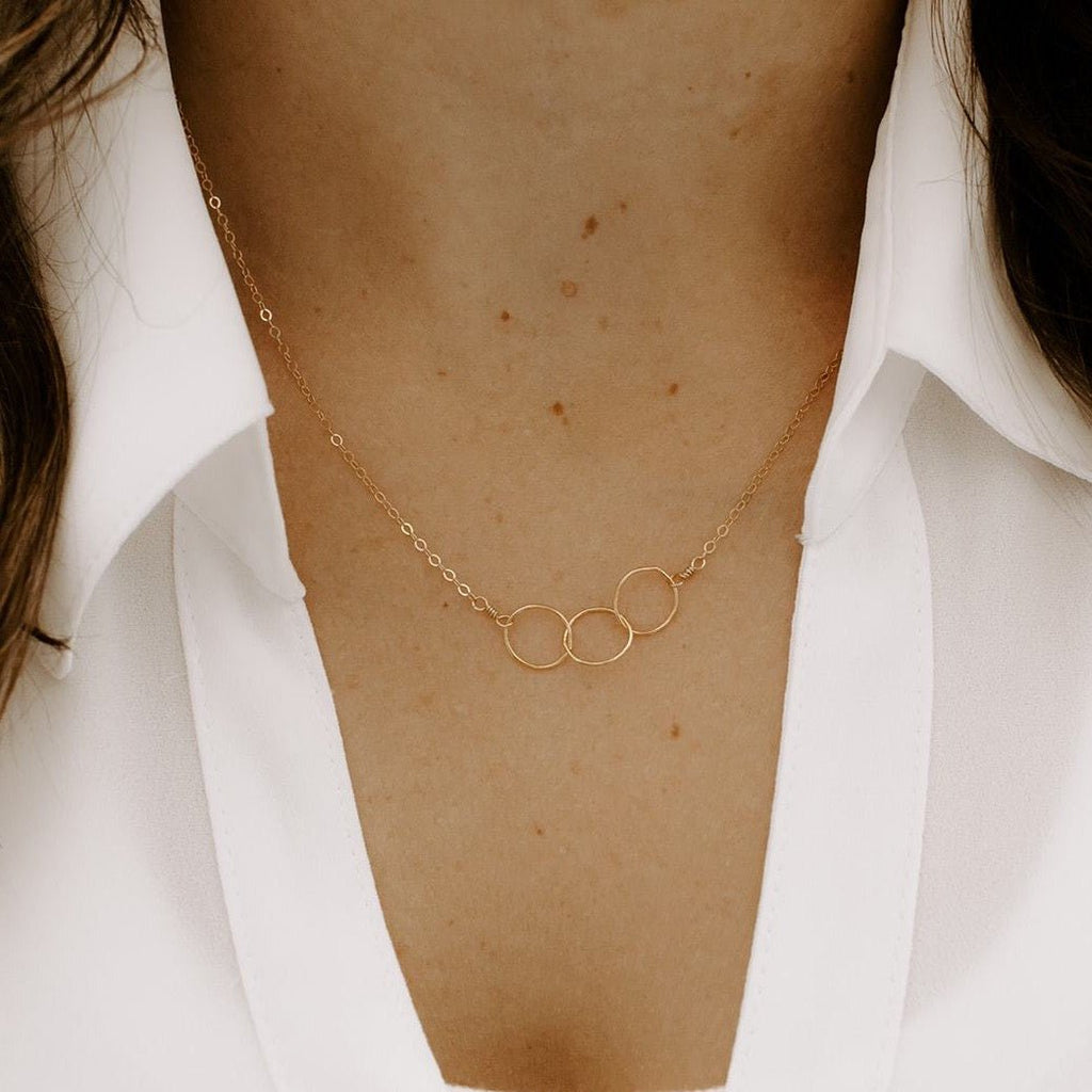 Close up of woman's neckline wearing white button down with gold necklace with 3 interlocking gold circles. Circles Necklace by Sarah Cornwell Jewelry