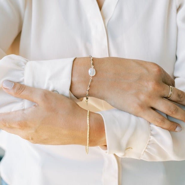 Woman's wrists crossed wearing cream blouse with gold rolo style chain bracelet, gold chain and white chalcedony bracelet and gold ring stack. Danny Bracelet by Sarah Cornwell Jewelry