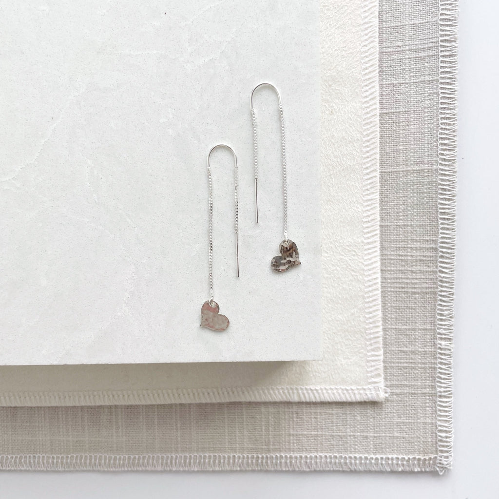 Silver chain threader earrings with a 2.25 inch drop and a tiny textured silver heart at the bottom. Darling Earrings by Sarah Cornwell Jewelry